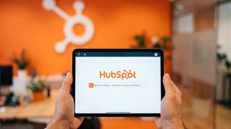 Vue subjective de mains tenant une tablette affichant l'utilisation de l'outil HubSpot AEO dans un bureau moderne.