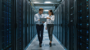 Deux techniciens étudient un workflow MLflow complexe sur un ordinateur portable, dans une salle de serveurs à la pointe de la technologie.